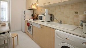 A compact kitchen with wooden cabinets, a microwave, a stove, a sink, and a washing machine. - Bright apartment in La Bourboule, 3 bedrooms, near center (La Bourboule)
