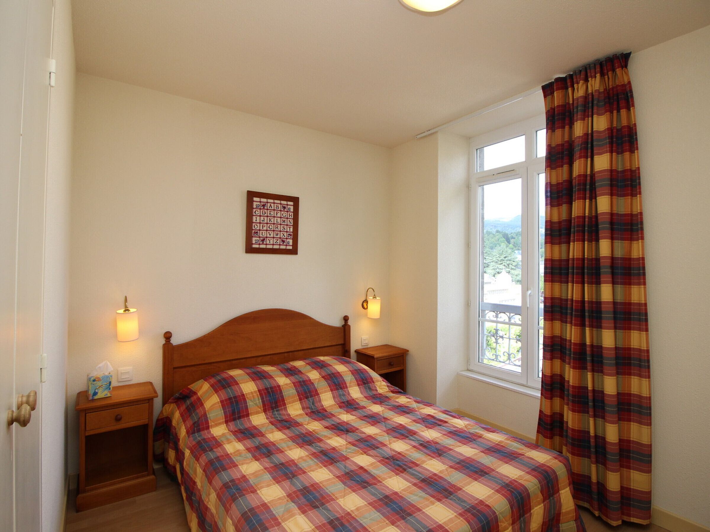 Une chambre à coucher avec un lit en bois, deux tables de chevet, une fenêtre avec des rideaux et un luminaire fixé au mur.