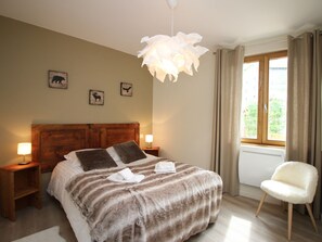 A bedroom with a wooden headboard, a large bed with a striped blanket, two bedside lamps, a white chair, and a window with curtains.