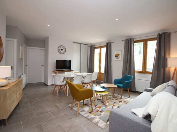 A modern living room with a sofa, a coffee table, and a TV. There is a dining area with chairs and a table. - LE MONT DORE - T3 Apartment with terrace, parking and wifi (Mont-Dore)