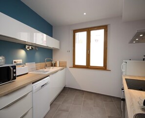 A modern kitchen with white cabinets, a microwave, a dishwasher, and a window with wooden frames.