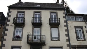 Un edifici de diverses plantes amb tres balcons, cadascun amb barana de ferro forjat i jardineres amb flors.