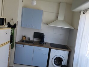 Une cuisine compacte équipée d’un lave-linge, d’un four à micro-ondes et de placards.