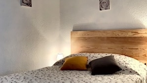Ein Schlafzimmer mit einem Holzkopfteil, einem Bett mit einem gemusterten Bettbezug, zwei Kissen und zwei an der Wand befestigten Bilderrahmen.