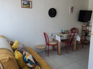 Un salon comprenant un canapé, une table à manger avec des chaises, une horloge et un téléviseur.