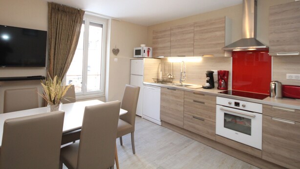 A modern kitchen with a dining area, a TV, and a window with curtains. - Mont-Dore: Central T3 Apartment with Wifi (Mont-Dore)