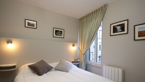 A hotel room with a large bed, two bedside tables, a window with curtains, and three framed pictures on the wall. - Mont-Dore: Central T3 Apartment with Wifi (Mont-Dore)