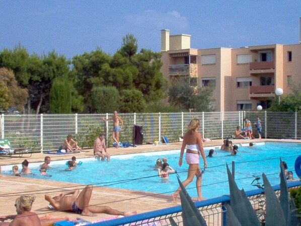 A swimming pool area with people sunbathing and swimming.