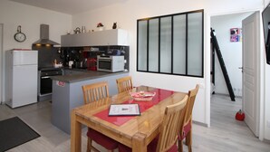 Eine kompakte Küche mit modernen Geräten, ein Essbereich mit einem Holztisch und Stühlen sowie ein großes Fenster mit satinierten Glasfeldern.