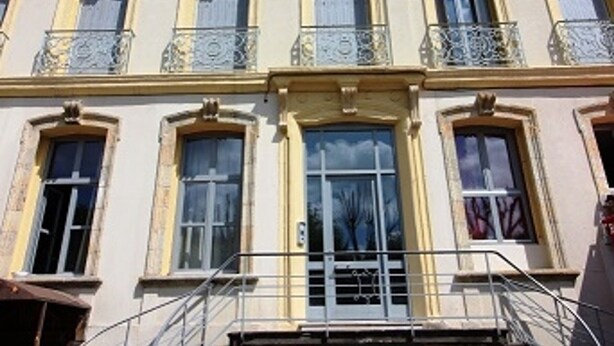 Ein mehrgeschossiges Gebäude mit einer symmetrischen Fassade, großen Fenstern und dekorativen Geländern.