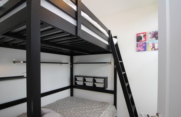 Een slaapkamer met stapelbed, een ladder, een plank met opbergdozen en een muur met vier kleurrijke schilderijen.