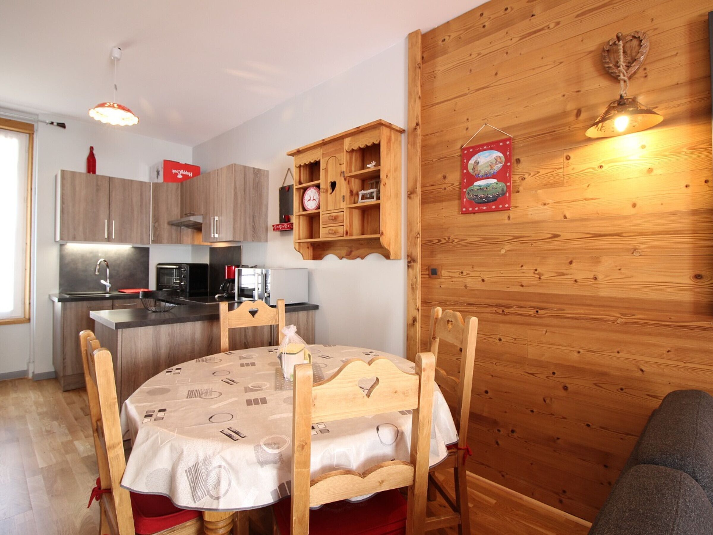 Een compacte keuken met moderne apparatuur, een eettafel met een tafelkleed met patroon en houten keukenkastjes.