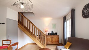 Una sala de estar con una escalera de madera, un sofá, una mesa de comedor con sillas y un aparador.