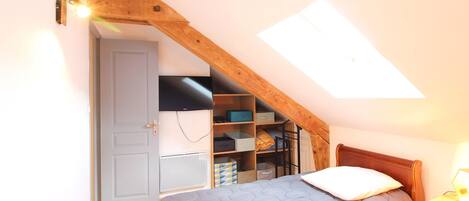 A bedroom with a sloped ceiling, a bed with a quilted cover, a bedside table with a lamp, and a built-in shelving unit with storage boxes.