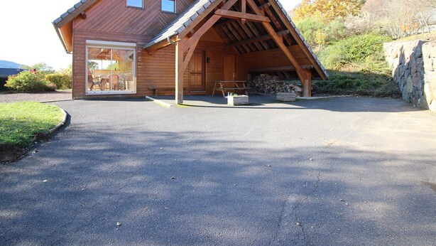 A wooden cabin with a sloped roof, a covered porch, and a stone wall. - Spacious 3* chalet with parking and WiFi in Mont Dore (Mont-Dore)