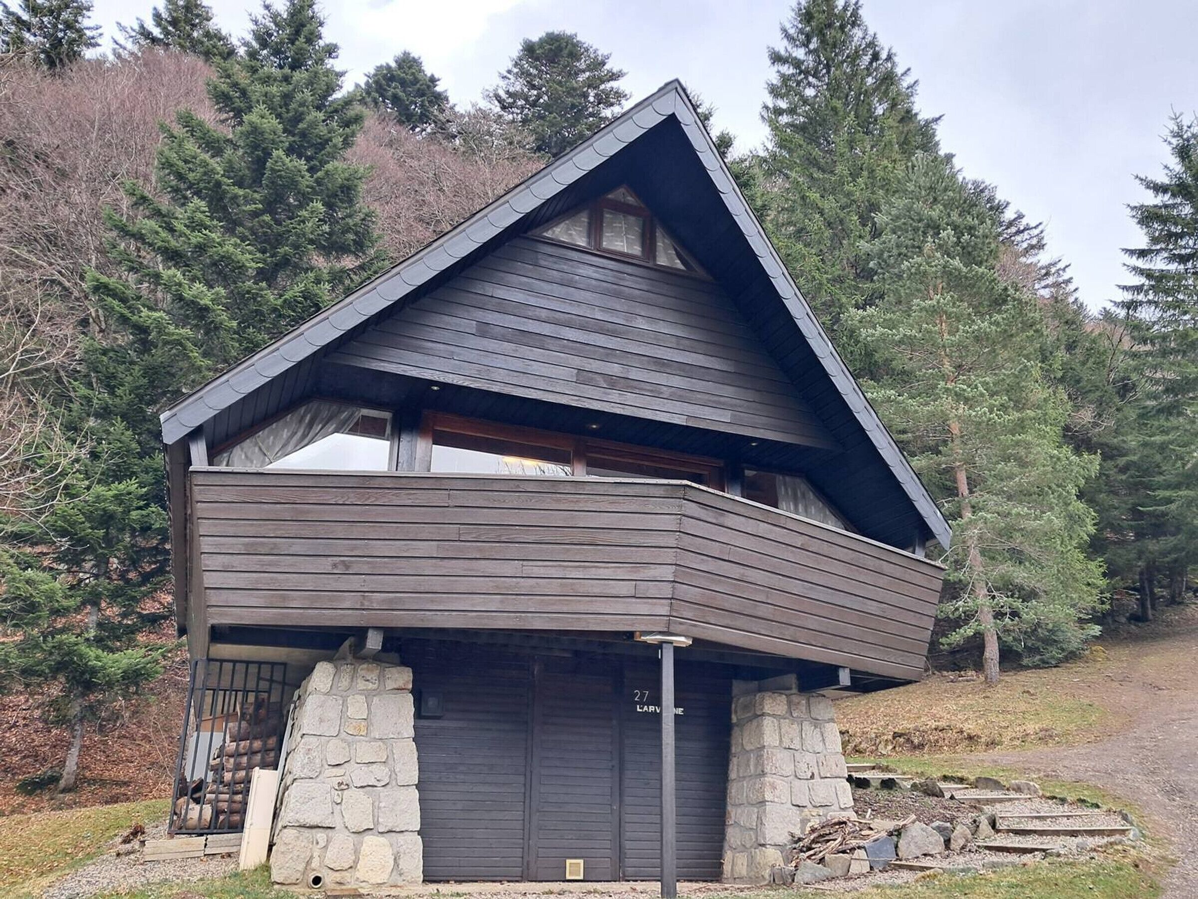 A modern log cabin with a stone foundation, a large garage door, and a steeply pitched roof.