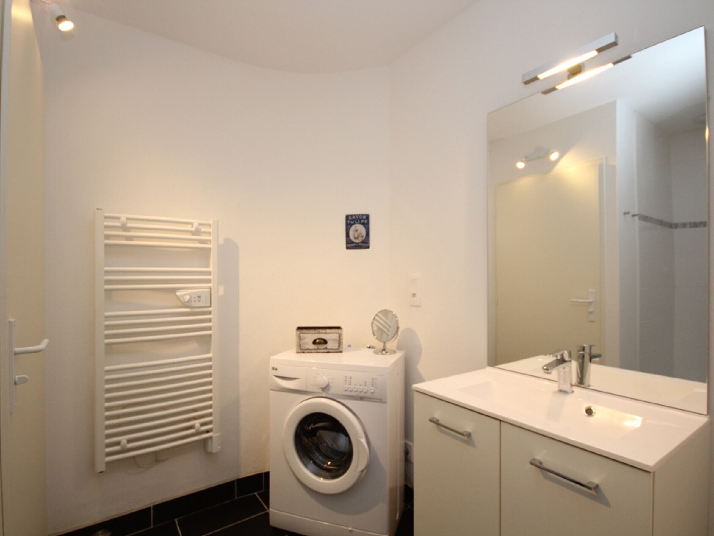 A compact bathroom with a washing machine, a sink, and a mirror.
