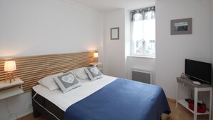 Ett sovrum med en säng, sänglampor, en tv på ett stativ, ett fönster med gardiner och en tavla på väggen.