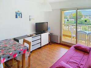 Una habitación con cama, escritorio con televisor, silla, mesa con mantel estampado y balcón con sillas.