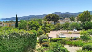 A residential area with a parking lot, a tall tree, and a view of the sea and hills in the background.