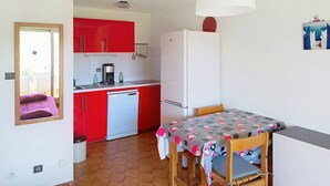 A compact kitchen with red cabinets, a white refrigerator, a coffee maker, and a dining table with a patterned tablecloth.
