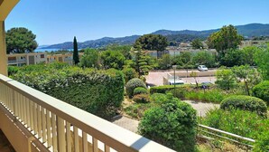 A balcony with a view of a landscaped area, buildings, and a distant coastline.