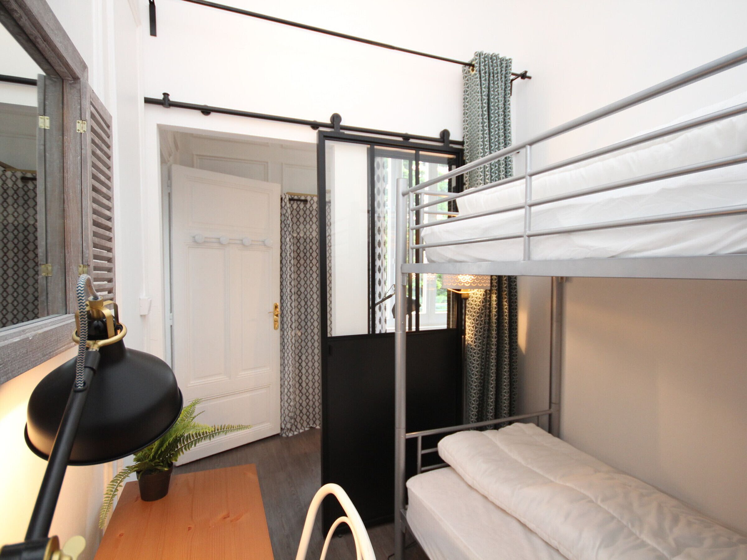 A compact room with a bunk bed, a desk with a lamp, and a potted plant.