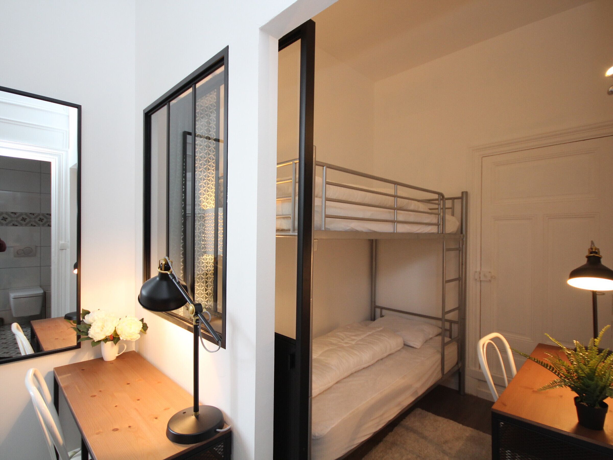 Een slaapkamer met stapelbed, bureau, stoel, lamp en een potplant.