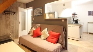 A cozy living area with a sofa, a dining table, and a kitchen in the background. - Beautiful T3 Duplex with Balcony, Wifi and Parking 300m from Center (Mont-Dore)