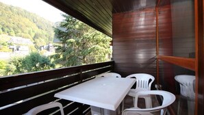 A balcony with a white table and chairs, overlooking a forested area with buildings in the distance. - Beautiful T3 Duplex with Balcony, Wifi and Parking 300m from Center (Mont-Dore)
