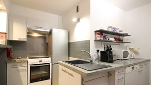A modern kitchen with white cabinetry, a built-in oven, a microwave, and a sink. There are shelves above the sink holding various kitchen items. - Beautiful T3 Duplex with Balcony, Wifi and Parking 300m from Center (Mont-Dore)