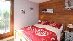A bedroom with a wooden headboard, a large window, and a bed with red bedding. - Charming T2 with balcony in Mont Dore, parking included (Mont-Dore)