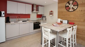 Une cuisine moderne avec des meubles blancs, une horloge murale en bois et un coin repas avec des chaises blanches.