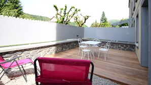 Une terrasse extérieure avec un mur en pierre, une plateforme en bois et un espace détente comprenant une table et des chaises.