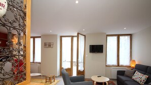 Un salon comprenant un canapé, un fauteuil, une petite table et un téléviseur fixé au mur.