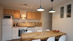 A compact kitchen with wooden cabinets, a microwave, a dishwasher, and a dining table with chairs. - Mont-Dore, renovated 2-bedroom with garden, parking, wifi (Mont-Dore)