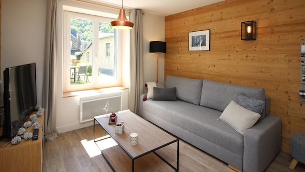 A modern living room with a grey sofa, a coffee table, a TV, and a wooden wall. - Mont-Dore, renovated 2-bedroom with garden, parking, wifi (Mont-Dore)