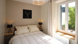 A bedroom with a bed, two bedside lamps, a wall-mounted light fixture, a framed deer head artwork, and a window with curtains. - Mont-Dore, renovated 2-bedroom with garden, parking, wifi (Mont-Dore)