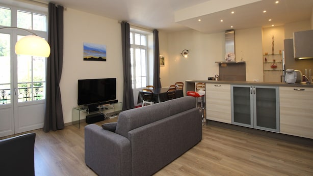 A modern apartment with a grey sofa, a TV, a dining area, and a kitchen. - LE MONT DORE - Spacious 2-Bedroom Apartment with Balcony and WIFI in Center (Mont-Dore)