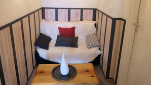 En mysig hörna med en vit, fluffig soffa, ett litet träbord med en vit vas och en tavla som hänger på väggen.