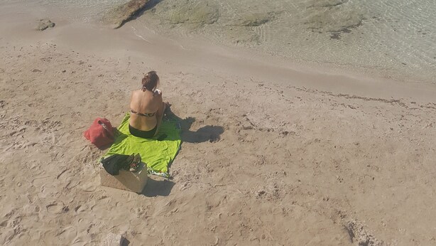 En strand med klart vatten, en vågbrytare av sten och fotspår i sanden.