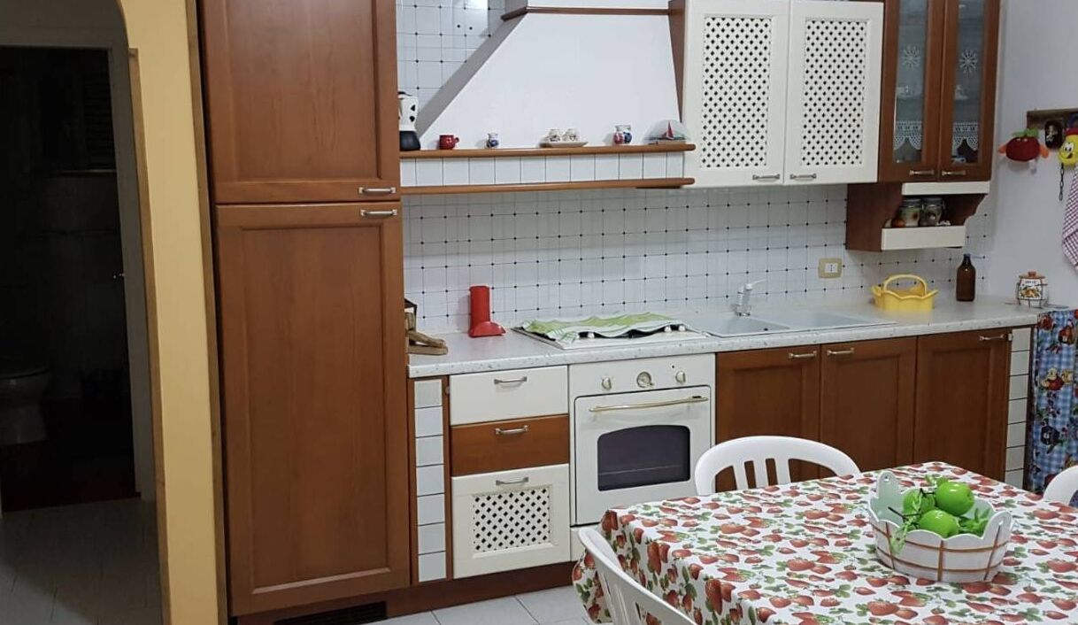 Una cocina con armarios de madera, un lavamanos, una estufa y una mesa con frutero.