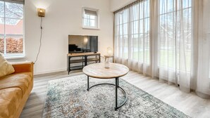 A modern living room with a sofa, a TV, a round coffee table, and large windows with sheer curtains. - Gorgeous home in Hoge Hexel with sauna (Hoge Hexel)