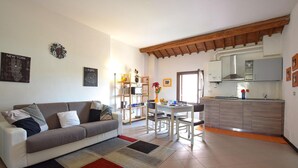 Una sala de estar con sofá, una mesa de centro y una zona de comedor con sillas y una mesa. Hay una cocina con armarios y una estufa.
