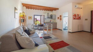 Una sala de estar con sofá, una mesa de comedor con sillas, una zona de cocina con armarios y un ventanal, además de un pasillo que da a un baño.