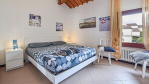 Un dormitorio con cama, mesitas de noche, una silla y una ventana con cortinas.