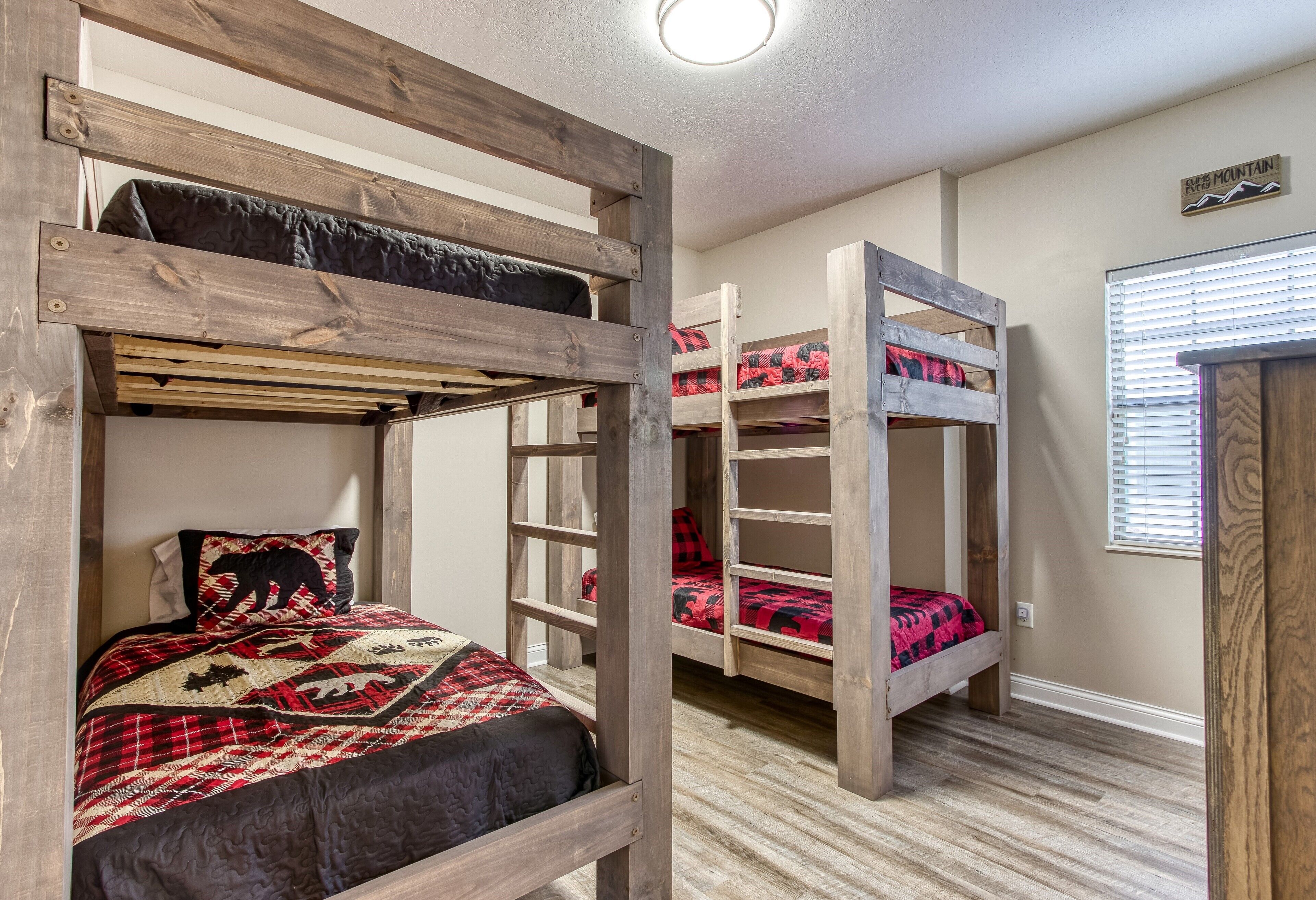 Ein Zimmer mit zwei Etagenbetten, eines mit Holzrahmen und das andere mit Metallrahmen. Rechts befindet sich ein Fenster mit Jalousien.