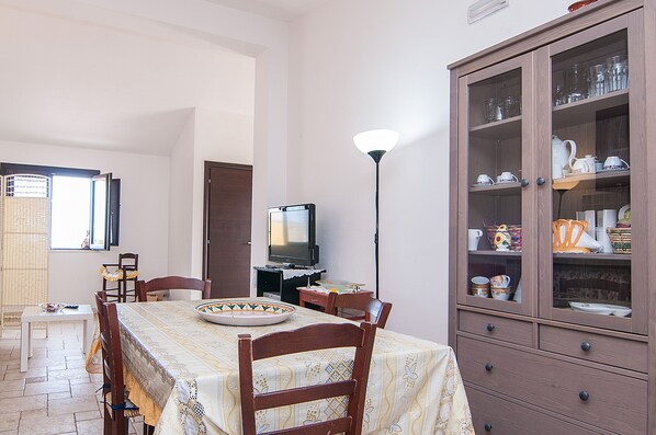 A dining area with a table set for four, a television, and a cabinet with glassware.