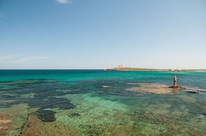 A coastal view with clear turquoise waters, a rocky outcrop, and a distant building on a small island.