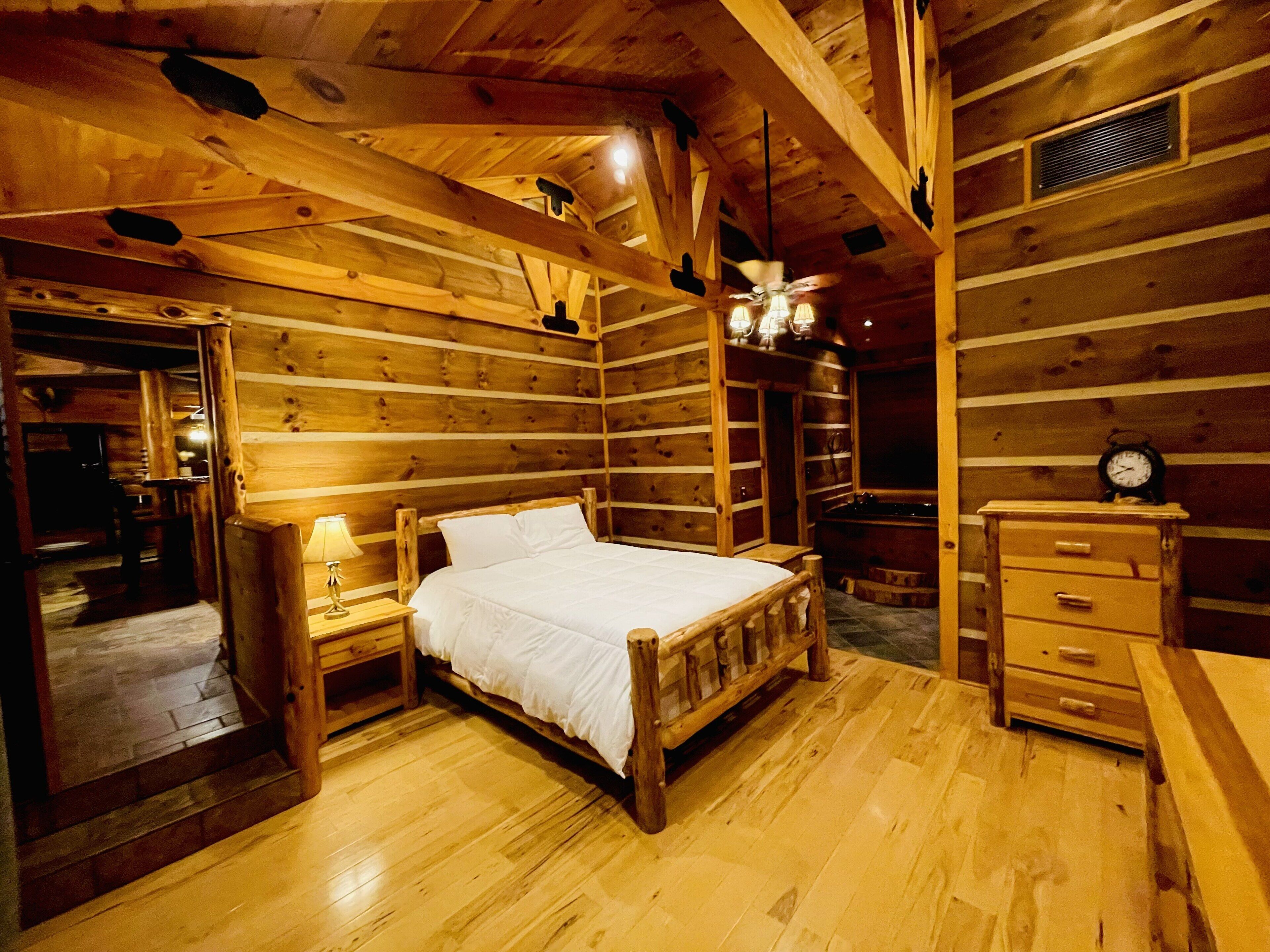 A wooden cabin bedroom with a bed, nightstand, dresser, and a ceiling fan.